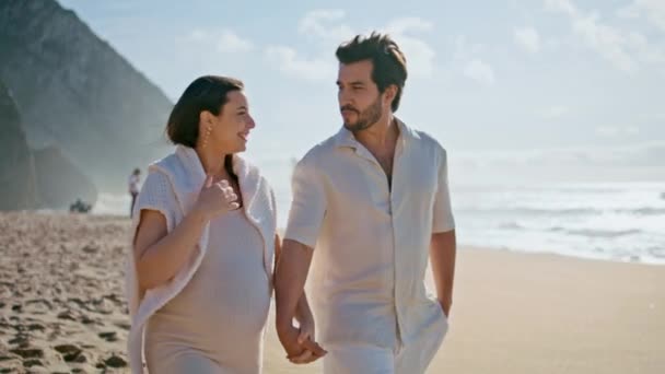 妊娠中の女性が日当たりの良い海岸で夫と一緒に歩き 一緒に笑っている 陽気な結婚したカップルは 夏のビーチで無料の遊歩道を楽しんでいます 赤ちゃんが幸せを感じるのを待っている笑顔の配偶者 — ストック動画