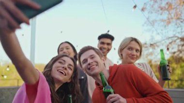 Neşeli arkadaşlar partide selfie çekiyorlar. Cep telefonu tutan mutlu kız akşam terasında fotoğraf çekiyor. Tasasız çeşitli öğrenciler çatıda hayatın tadını çıkarıyorlar. Halk yaşam tarzı konsepti