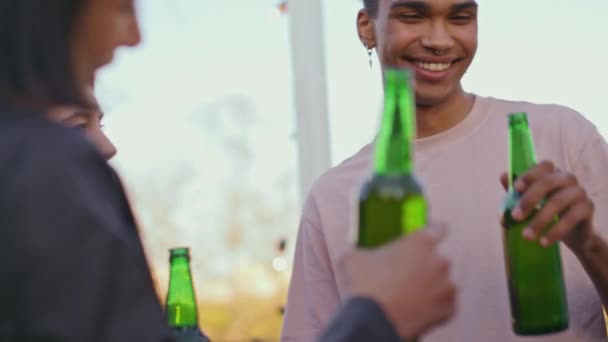 不同的朋友在屋顶派对特写处为啤酒欢呼 在夏天的露台上 队友们笑着敲击着酒瓶 快乐的嬉皮士聚在一起快乐的男孩和女孩喝饮料 — 图库视频影像