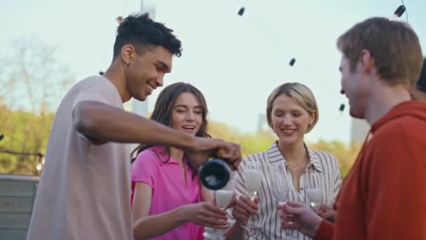 非洲家伙倒香槟在屋顶企业活动特写 多种族的朋友在露天平台上庆祝相遇 享受着灿烂的葡萄酒 年轻人在一起很开心党的概念 — 图库视频影像