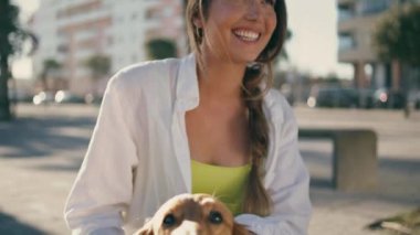 Mutlu bayan yaz tatilinin tadını çıkarıyor. Gülümseyen kadın, Sunny Caddesi 'nde rahatlayan sevimli köpeğe sarılıyor. Pozitif öğrenci kızı evcil hayvanı öpüyor. Yumuşak kürkünü okşuyor. Yaz eğlencesi konsepti