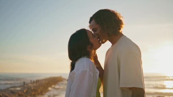 夜の海岸でキスをするテンダーカップル 笑顔の女性は愛で互いを見つめあっている 日没の海岸で鼻に触れる幸せなペアはズームアウトします 人間関係を愛する 幸福のコンセプト — ストック動画