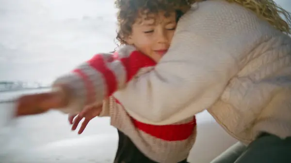 Playful boy running mother on ocean shore. Happy parent woman hug spinning child in autumn sunlight. Cheerful family enjoying weekend spending time together. Caring parenthood mothers day concept.
