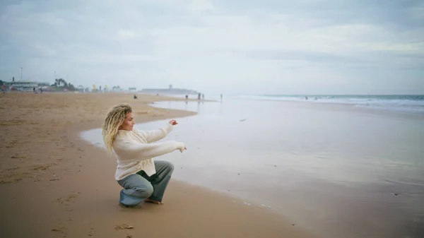 Woman throwing stones water ocean on cloudy day. Thinking girl resting seaside contemplating life alone. Beautiful serene person tourist enjoying autumn weekend at sea. Dreamy peaceful mood concept.