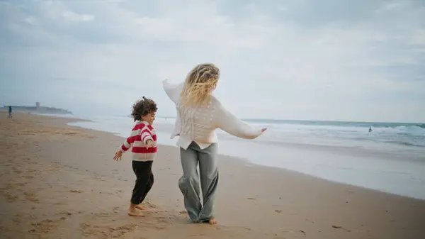 Family playing airplane pilot on autumn ocean shore. Joyful mother son running beach having fun together on weekend. Adorable curly boy catching hug young mom. Playful parent enjoying time with child.