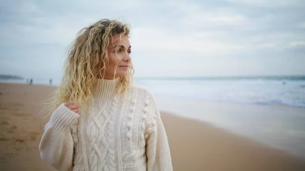 Gorgeous female looking ocean view on autumn holiday. Romantic woman resting outdoors enjoying seaside in warm knitted sweater. Smiling blonde thinking feeling satisfied with life. Calm mood concept.
