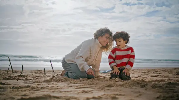 Young mom kissing child on weekend holidays. Happy parent building sand castle with adorable little son. Affectionate mother babysitter express love enjoy beach vacation. Caring relationships concept