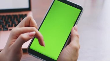 Modern iş yerinde yeşil ekranlı akıllı telefon kullanan tanınmayan bir kadın. Krom tuşlu telefondan kız elleri kayıyor. Bilinmeyen bayan evde mobil bankacılık uygulaması arıyor.