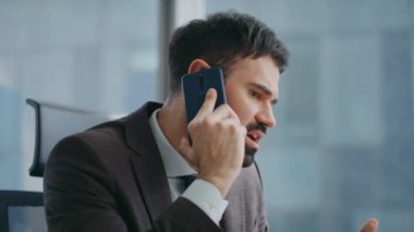 İş adamı telefon konuşmalarında çalışıyor modern ofisi kapatıyor. Ciddi bir özgüvenli şirket yöneticisi akıllı telefon ile iş meselelerini çözüyor. Sakallı girişimci konuşuyor..