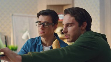 Odaklanmış tasarımcılar vitrindeki yiyecekleri yakın çekimde gösteriyorlar. İki adam öğle yemeği molasında proje tartışıyorlar. Yaratıcılar iş yerinde aromatik sandviçlerin tadını çıkarırken fikirleri paylaşıyorlar.