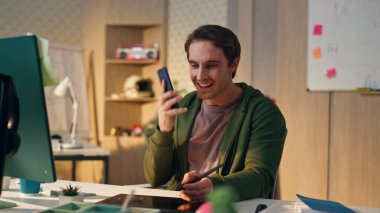 İş yerindeki cep telefonu çizim tabletine cevap veren mutlu bir sanatçı. Ofiste çalışırken cep telefonuyla konuşan yaratıcı gülümseyen web tasarımcısı. Bilgisayarın başında oturan rahat adam 
