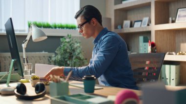 Bilgisayar masasında defter sayfaları çevirmekle meşguldüm. Yaratıcı iş adamını kapatın ve özel dolapta kahve yudumlayan gerekli notları arayın. Modern ofiste sakince çalışan ciddi bir adam.