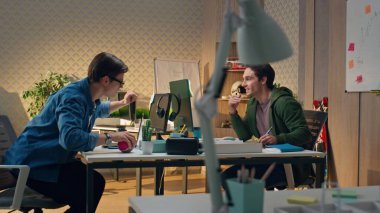 Ofiste çalışan genç iş adamları birlikte iletişim kuruyor. Gözlüklü adam gülümseyen meslektaşına soru soruyor. Web tasarımcısı yaratıcı iş yerinde röntgenci bilgisayar ekranı. İş arkadaşları fikir alışverişinde bulunuyor.