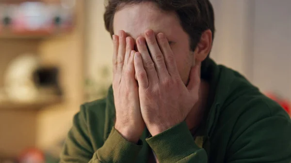 Disappointed man covering face palm thinking in home office closeup. Stressed creator worried project fault working at modern interior. Tired overworked designer rubbing eyes with sad emotions at work