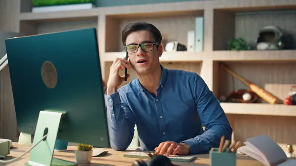 Happy startuper speaking smartphone in office. Close up successful freelancer ending call picking mobile phone down at modern interior. Eyeglasses man watching computer screen at empty cabinet