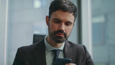 Ciddi bir iş adamı iş yerindeki telefon ekranına bakıp iş mesajlarını okuyor. İş için mobil uygulama kullanan odaklanmış sakallı işçinin portresi. Akıllı ofis yöneticisi telefonla çalışır.