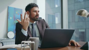 Düşünceli iş adamı videosu arıyor. Lüks ofis oturma stratejisini düşünüyor. Ciddi sakallı patron internetteki pazarlıkta dizüstü bilgisayarla konuşuyor. Web kamerası kullanılarak başarılı bir ceo