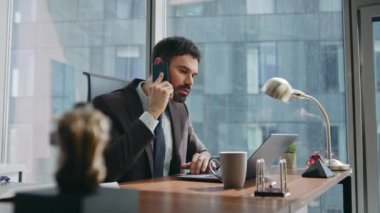 Profesyonel danışman modern ofis masasında oturup laptopa yakından bakıyor. Ciddi, kendine güvenen iş adamı bilgisayardaki telefon okuma raporuyla işi tartışıyor. İş iletişimi