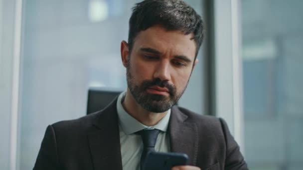 真剣なビジネスマンは 会社の職場でビジネスメッセージを読む電話スクリーンを見ています 仕事のためのモバイルアプリを使用して焦点を当てたひげ付き労働者の肖像画 スマートなオフィスのマネージャーは電話で働きます — ストック動画