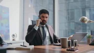 Tatmin olmamış girişimci gergin bir şekilde ofis masasında dizüstü bilgisayarla akıllı telefon konuşuyor. Kızgın yönetici, iş yerindeki telefon konuşmasında kavga ediyor. Patron stresten telefonda konuşuyor..