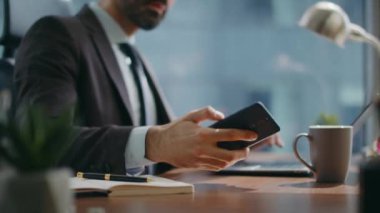 Masada dizüstü bilgisayar yazan bir ofis çalışanı akıllı telefon ekranına yakından bakıyor. Kendine güveni tam bir yönetici modern işyerindeki iş görüşmelerine cevap veriyor. Telefonla konuşan başarılı bir çalışan..