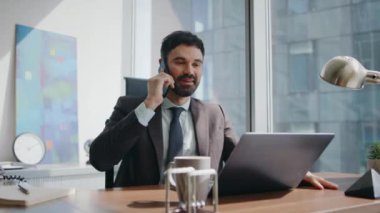 Gülümseyen yönetici modern ofis masasında oturan müşteriyi arıyor. Mutlu iş adamı iş yerinde hoş bir telefon görüşmesi yapıyor. Neşeli sakallı şirket çalışanı iş molasında telefonla konuşuyor.