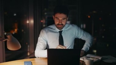 Başarılı iş adamı gece geç saatlerde modern ofiste tek başına çalışıyor. Çekici sakallı menajer dizüstü bilgisayarda tatmin edici iş sonuçları arıyor. Kendine güveni olan girişimci çalışma masasında oturuyor..