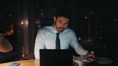 Stresli, geç saatlere kadar çalışan, şirket işyerinde oturan dizüstü bilgisayarlı monitörü yakından izleyen. Endişeli iş adamı iş sorununu çözmeye çalışıyor. Endişeli adam ofis müdürü gece çalışan notları kontrol ediyor..
