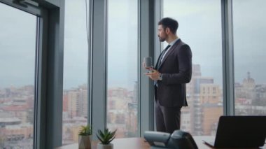 Başarılı bir işadamı, vitrindeki lüks ofiste kahve içiyor. Sakallı, dalgın CEO iş yerinde sıcak içecekten hoşlanır. Rahatlamış takım elbiseli adam bulutlu şehir manzarasına bakıyor..