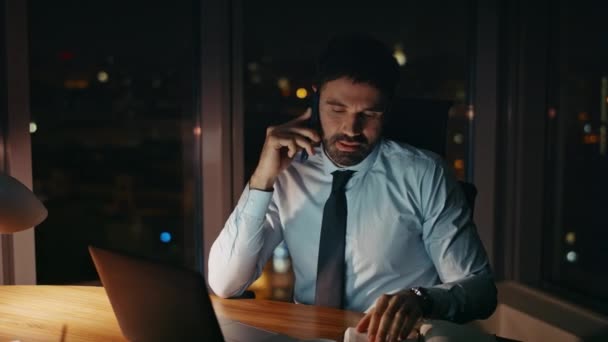 男人工作狂般的会说话的电话坐在写字台旁 手提电脑也在旁边 疲惫过度劳累的商人深夜在电话机上讨论工作问题 认真工作的员工 — 图库视频影像