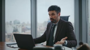 Video konferansına bağıran bir iş adamı modern ofiste oturarak şirketin finansal kaybından memnun değil. Kızgın sakallı yönetici internette dizüstü bilgisayarla tartışıyor. Web kamerasında şikayet eden üzgün bir adam..