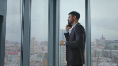 Ofis panoramik penceresinde duran iş adamı telefon görüşmeleri hakkında konuşuyor. Güvenilir sakallı yönetici iş görüşmesinde ortaklarla konuşuyor. Ciddi bir adam telefonda işi tartışıyor..