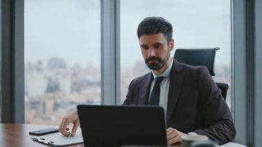 Sakallı patron bilgisayar ekranı görünümlü çalışma belgesini kapatıyor. Başarılı, zeki iş adamı, iş kararına imza atıyor. Lüks ofis masasında oturan ciddi bir CEO..