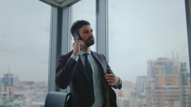 Ofis panoramik penceresinde şık bir takım elbiseyle telefonla konuşan bir iş adamı. Başarılı yönetici iş yerinden ortakları arıyor. Güvenilir erkek işçi telefonda müşteriye danışıyor.
