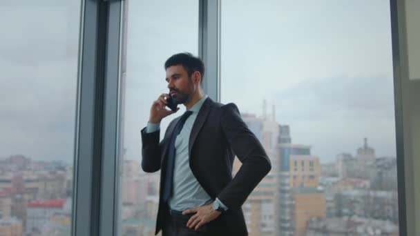 忙碌的Ceo呼叫合作伙伴站在豪华办公室窗口 有胡子的公司经理在工作场所用智能手机进行商务对话 自信聪明的老板通过电话分配工作任务 — 图库视频影像