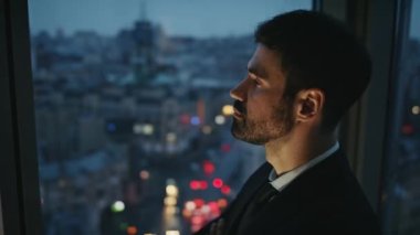 Ofis panoramik penceresinde tek başına duran düşünceli bir iş adamı. Yakışıklı sakallı girişimci portresi. Gece kasabasını seyrediyor, kariyer düşünüyor. Çalışma konsepti.