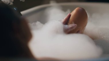 Nazik model akşam tuvaletinde spa prosedürlerini uyguluyor. Sakin bir kadın evinde bacağına dokunup köpük banyosu yapıyor. İçerideki köpüklü suda dinlenen seksi, şehvetli kadın. Güzellik rutini konsepti