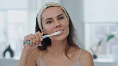 Banyo pov videosundaki mutlu kadın diş hijyeni rutini. Esmer, gülümseyen, dişlerini fırçalayan bir kadın. Güzel kız diş macunuyla ağzını temizleyip plaket portresini çıkarıyor. Taze gülümseme konsepti