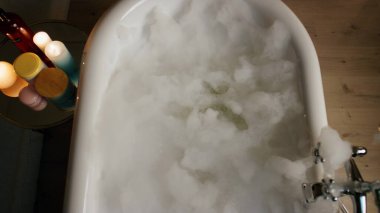 Mum odası manzaralı lüks küvet köpüklü su. Akşam, pahalı otel odalarında köpükler banyosunu doldurdu. Evde seramik mobilyalarda sıcak sabun sıvısı. Spa prosedürleri ve güzellik rutini kavramı