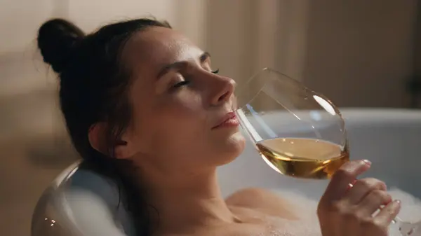 Sexy woman sipping champagne at luxury bathroom closeup. Sensual girl relaxing wine glass chilling foamy bathtub. Dreamy model drinking alcohol enjoying leisure at candles home. Beauty and wellness