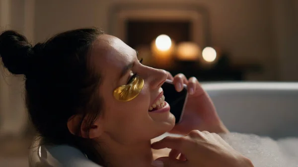Laughing model talking smartphone in bathtub closeup. Relaxed happy girl laying hot bubbled bath speaking cellphone. Cheerful woman gossiping mobile phone smiling at home. Domestic spa procedures