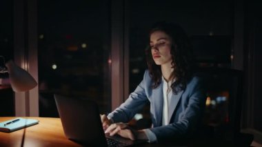 Ofis çalışanı akşam geç saatlerde dizüstü bilgisayar ekranı karşısında umutsuzluk içinde oturuyor. Fazla mesai yapan iş kadını, karanlık işyerinde fazla mesai yapmaktan yoruldu. Yorgun bayan yönetici son teslim tarihini yapıyor..
