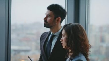 Ofis koridorunda iletişim kuran iki takım arkadaşı panoramik pencereyi kapatıyor. Kendine güvenen bir iş kadını ciddi sakallı bir yöneticiyle iş hakkında konuşuyor. İş stratejisini tartışan iki meslektaş.