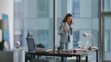 Ofis masasının yanında bekleyen mutlu yönetici çağrıya cevap veriyor. Gülümseyen iş kadını iş yerinde hoş bir telefon konuşması yapıyor. Zarif bayan CEO, akıllı telefon konuşmasında iyi haberler duymaktan memnun..