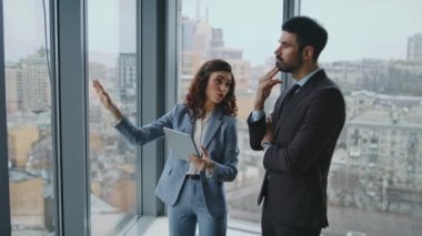 Meslektaşlar panoramik pencerede durup şehir manzarasına bakarak fikir paylaşıyorlar. Ofis koridorunda inşaat planını tartışan kendine güvenen iş arkadaşları. Tabletli akıllı kadın yöneticiye çalışma sürecini açıklıyor