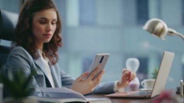 Patroniçe, iş yerindeki akıllı telefonlara bakıyor. Kendine güvenen iş kadını cep telefonuyla modern ofiste iş hakkında konuşuyor. Gülümseyen genç kız yönetici telefonda konuşuyor..