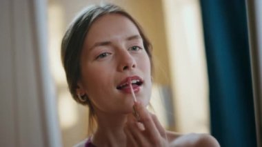 Yakından bakınca güzel bir kız dudak boyuyor. Aynaya bakan çekici bir kadın evde romantik makyaja hayran. Gülümseyen güzel bayan ruj sürerek makyaj yapıyor. Kendine güvenen zarif bir kadın..