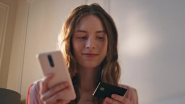 Genç bir kadın kredi detaylarını gün ışığında yakından giriyor. İnternetten alışveriş yapan gülümseyen kız evde ödeme doğrulaması yapıyor. Mutlu gevşemiş genç akıllı telefon plastik kartı alır. Siber düzen bankacılığı