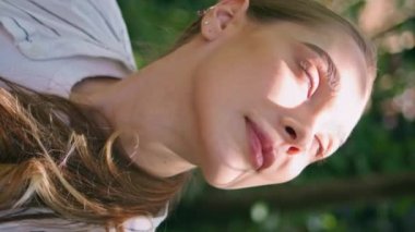 Kapalı, sakin kadın yaz güneşinin altında orman yeşilliklerinde parlıyor. Güzel parktaki doğa güzelliğine bakan mutlu nazik kızın portresi. Sakin bir bayan bahçede dikey olarak dinleniyor.