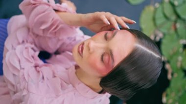 Gölde oturan görkemli kadın yeşil nilüferlerle kaplanmış. Mistik kız portresi, doğa göleti dikey videosuna bakıyor. Büyülü nehir manzarasında poz veren güzel bir fantezi modeli..